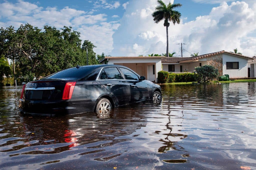A car sits in water halfway up its wheels near a home