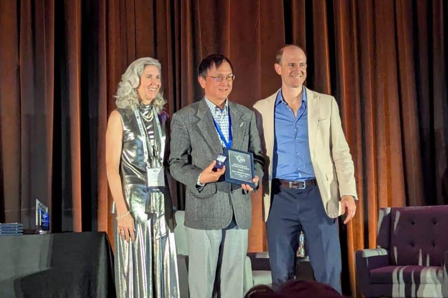 Kenny Cheng holds an award plaque while standing between two other people.