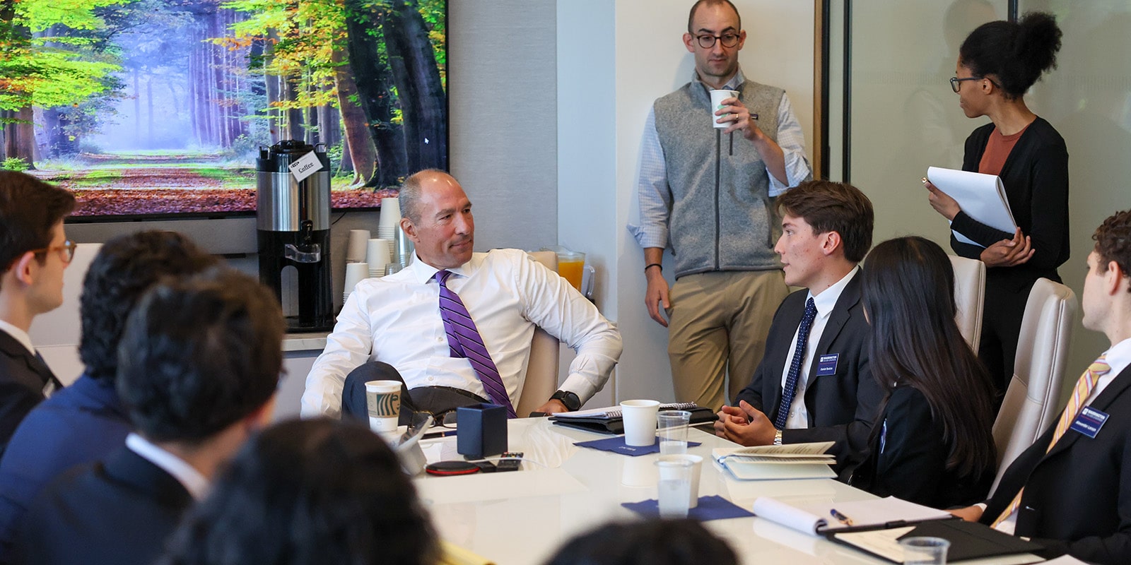 Finance students sitting around a table and talking to an older professional.